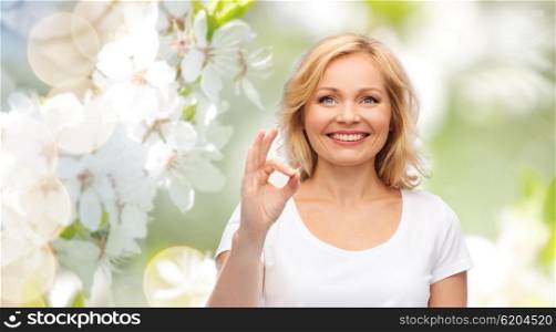 gesture, advertisement and people concept - smiling woman in blank white t-shirt showing ok hand sign over natural spring cherry blossom background