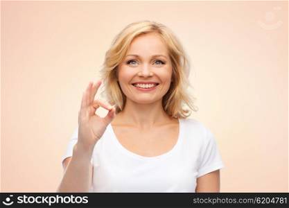 gesture, advertisement and people concept - smiling woman in blank white t-shirt showing ok hand sign over beige background