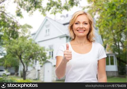 gesture, advertisement, real estate, home and people concept - smiling woman in blank white t-shirt showing thumbs up over private house background