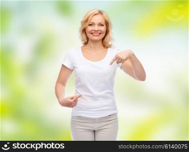 gesture, advertisement, summer and people concept - smiling woman in blank white t-shirt pointing finger to herself over green natural background