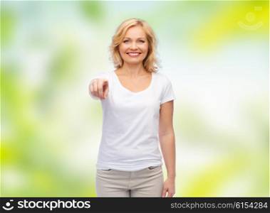 gesture, advertisement, summer and people concept - smiling woman in blank white t-shirt pointing finger to you over green natural background