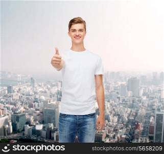 gesture, advertising and people concept - smiling young man in blank white t-shirt showing thumbs up over city background