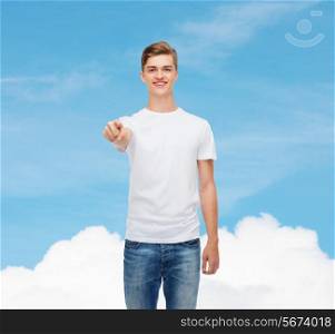 gesture, advertising, dream and people concept - smiling young man in blank white t-shirt pointing at you over blue sky background
