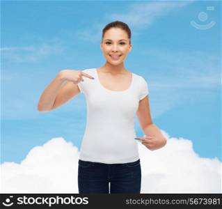 gesture, advertising, dream and people concept - smiling young woman in blank white t-shirt pointing fingers on herself over blue sky background
