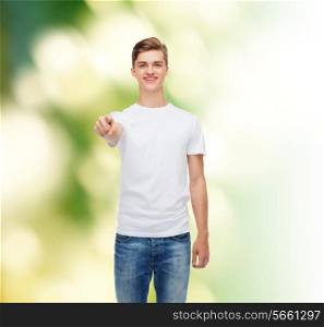 gesture, advertising, ecology and people concept - smiling young man in blank white t-shirt pointing at you over green background