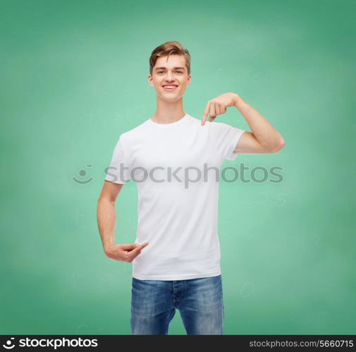 gesture, advertising, education, school and people concept - smiling young man in blank white t-shirt pointing fingers on himself over green board background