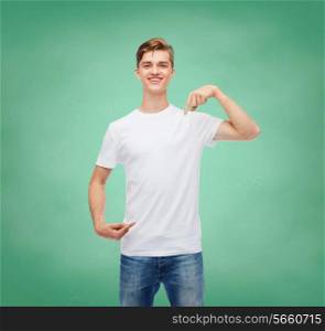gesture, advertising, education, school and people concept - smiling young man in blank white t-shirt pointing fingers on himself over green board background