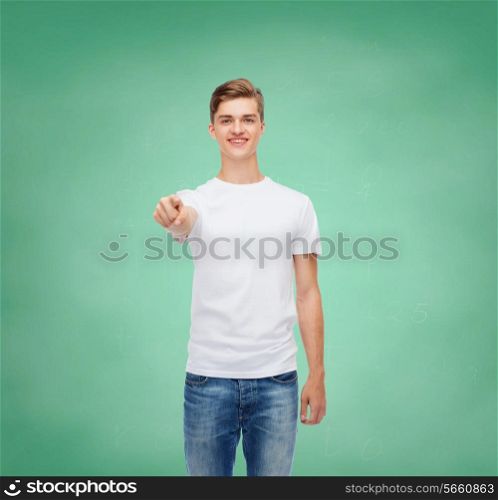 gesture, advertising, education, school and people concept - smiling young man in blank white t-shirt pointing at you over green board background