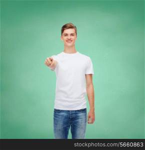 gesture, advertising, education, school and people concept - smiling young man in blank white t-shirt pointing at you over green board background