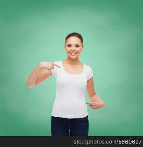 gesture, advertising, education, school and people concept - smiling young woman in blank white t-shirt pointing fingers on herself over green board background
