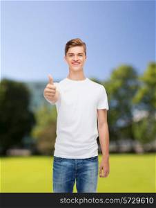 gesture, advertising, summer vacation and people concept - smiling young man in blank white t-shirt showing thumbs up over park background