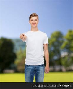 gesture, advertising, summer vacation and people concept - smiling young man in blank white t-shirt pointing at you over park background