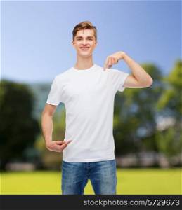 gesture, advertising, summer vacation and people concept - smiling young man in blank white t-shirt pointing fingers on himself over park background