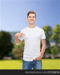gesture, advertising, summer vacation and people concept - smiling young man in blank white t-shirt pointing finger on himself over park background