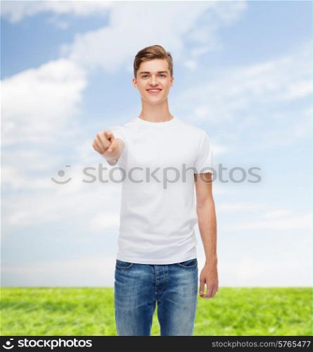 gesture, advertising, summer vacation and people concept - smiling young man in blank white t-shirt pointing at you over natural background