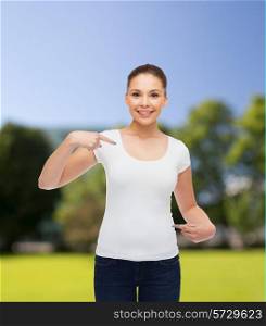 gesture, advertising, summer vacation and people concept - smiling young woman in blank white t-shirt pointing fingers on herself over park background