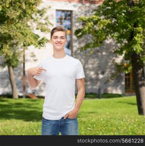 gesture, advertising, summer vacation, education and people concept - smiling young man in blank white t-shirt pointing finger on himself over campus background