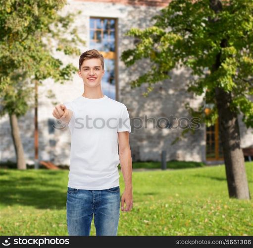 gesture, advertising, summer vacation, education and people concept - smiling young man in blank white t-shirt pointing at you over campus background