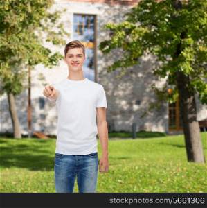 gesture, advertising, summer vacation, education and people concept - smiling young man in blank white t-shirt pointing at you over campus background