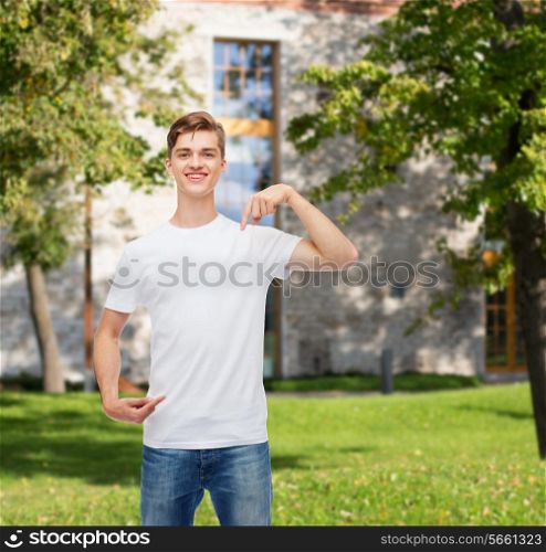 gesture, advertising, summer vacation, education and people concept - smiling young man in blank white t-shirt pointing fingers on himself over campus background