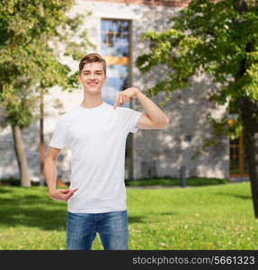 gesture, advertising, summer vacation, education and people concept - smiling young man in blank white t-shirt pointing fingers on himself over campus background