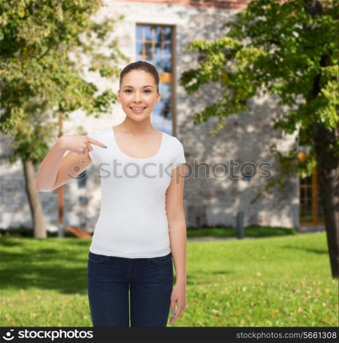 gesture, advertising, summer vacation, education and people concept - smiling young woman in blank white t-shirt pointing finger on herself over campus background
