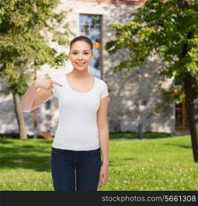 gesture, advertising, summer vacation, education and people concept - smiling young woman in blank white t-shirt pointing finger on herself over campus background