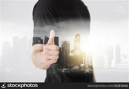 gesture and people concept - close up of man hand showing thumbs up over city with double exposure. man showing thumbs up