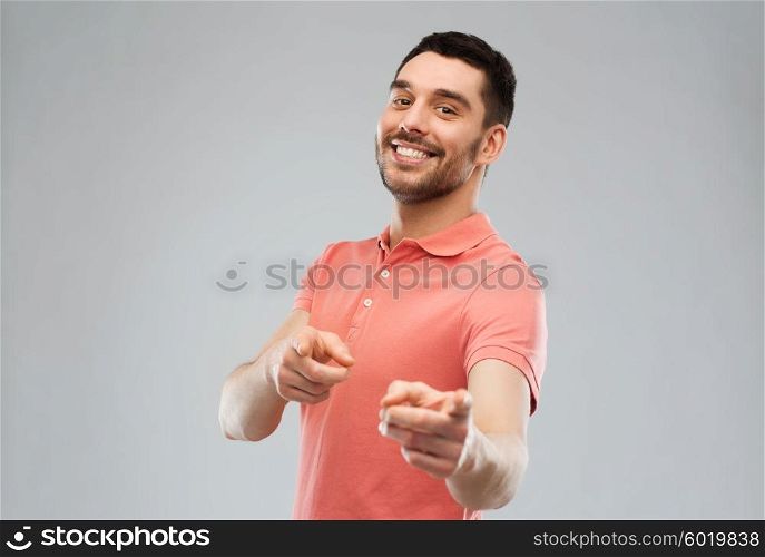 gesture and people concept - happy smiling young man pointing finger to you over gray background. man pointing finger to you over gray background