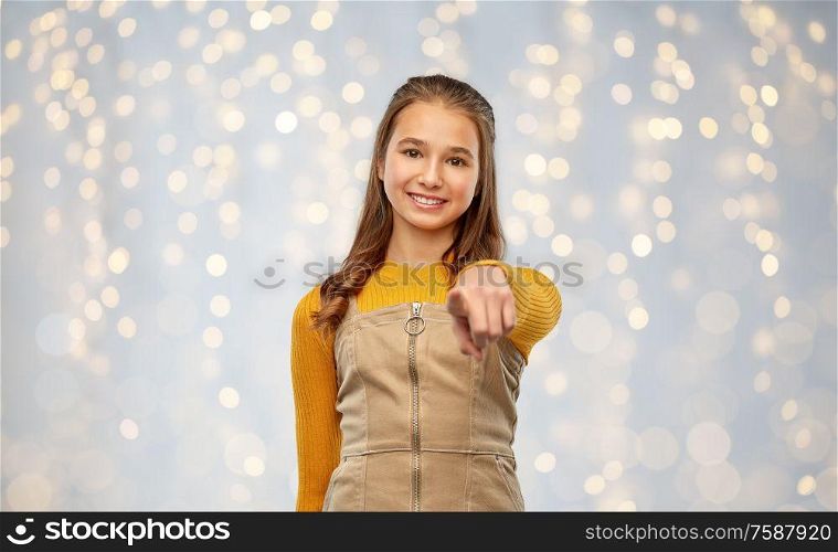 gesture and people concept - happy smiling young teenage girl pointing to camera over festive lights background. smiling young teenage girl pointing to camera