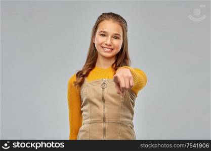 gesture and people concept - happy smiling young teenage girl pointing to camera over grey background. smiling young teenage girl pointing to camera