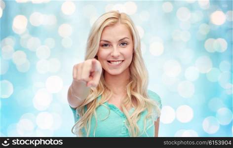 gesture and people concept - happy smiling young woman or teenage girl pointing finger to you over blue holidays lights background. happy young woman pointing finger to you