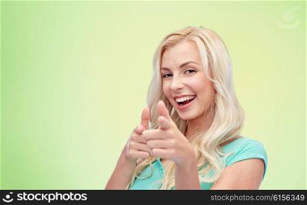 gesture and people concept - happy smiling young woman or teenage girl pointing finger to you over green natural background. happy young woman pointing finger to you