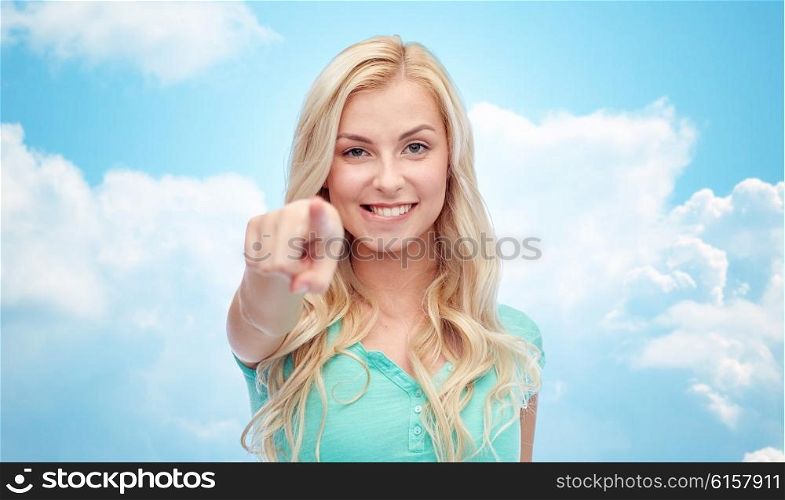gesture and people concept - happy smiling young woman or teenage girl pointing finger to you over blue sky and clouds background. happy young woman pointing finger to you