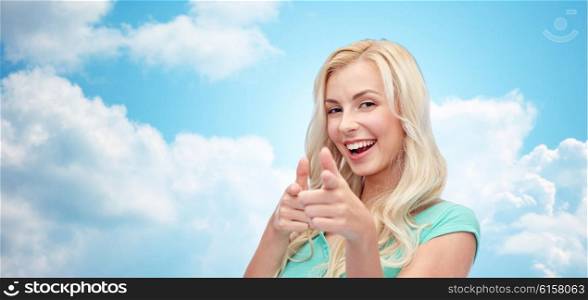 gesture and people concept - happy smiling young woman or teenage girl pointing finger to you over blue sky and clouds background. happy young woman pointing finger to you