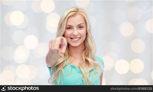 gesture and people concept - happy smiling young woman or teenage girl pointing finger to you over holidays lights background. happy young woman pointing finger to you