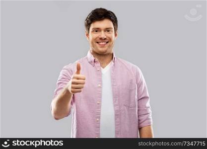 gesture and people concept - happy young man showing thumbs up over grey background. happy young man showing thumbs up