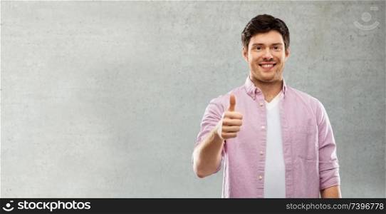 gesture and people concept - happy young man showing thumbs up over grey background. man showing thumbs up over grey concrete wall