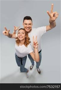 gesture and people concept - portrait of happy couple in white t-shirts showing peace over grey background. happy couple in white t-shirts showing peace
