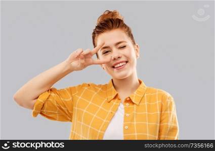 gesture and people concept - smiling red haired teenage girl in checkered shirt showing peace hand sign over grey background. smiling red haired teenage girl showing peace