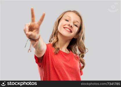 gesture and people concept - smiling teenage girl with long wavy hair in red t-shirt showing peace hand sign over grey background. smiling teenage girl in red t-shirt showing peace