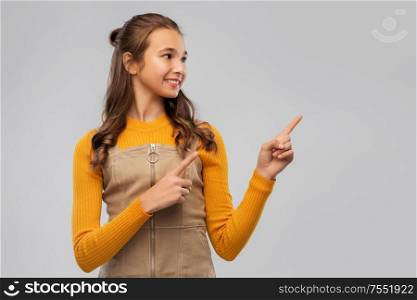 gesture and people concept - smiling teenage pointing fingers up girl over grey background. young teenage girl pointing fingers up