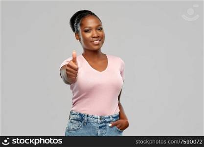 gesture and people concept - smiling young african american woman showing thumbs up over grey background. happy african american woman showing thumbs up