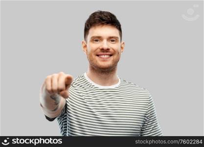 gesture and people concept - smiling young man in striped t-shirt pointing finger to camera over grey background. man in yellow sweatshirt pointing finger to camera