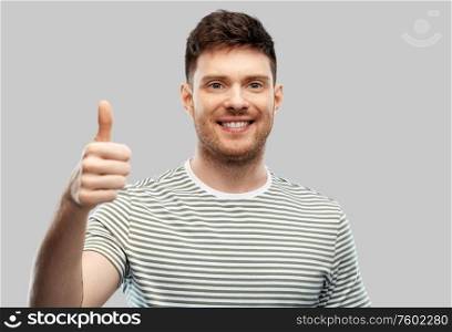 gesture and people concept - smiling young man in striped t-shirt showing thumbs up over grey background. smiling young man showing thumbs up