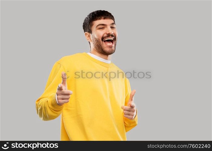 gesture and people concept - smiling young man in yellow sweatshirt showing thumbs up over grey background. smiling young man showing thumbs up