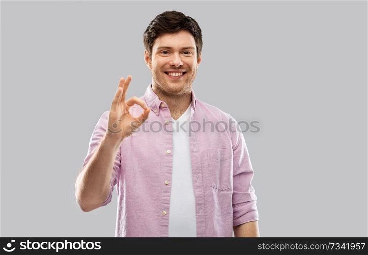 gesture and people concept - smiling young man showing ok hand sign over grey background. smiling young man showing ok hand sign