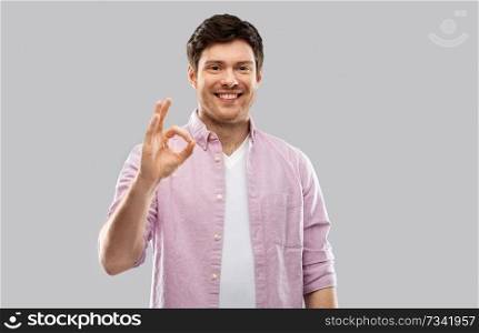gesture and people concept - smiling young man showing ok hand sign over grey background. smiling young man showing ok hand sign