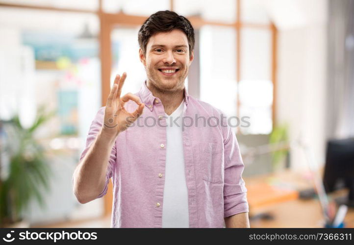 gesture and people concept - smiling young man showing ok hand sign over office room background. smiling young man showing ok hand sign over office