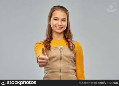 gesture and people concept - smiling young teenage girl showing thumbs up over grey background. young teenage girl showing thumbs up